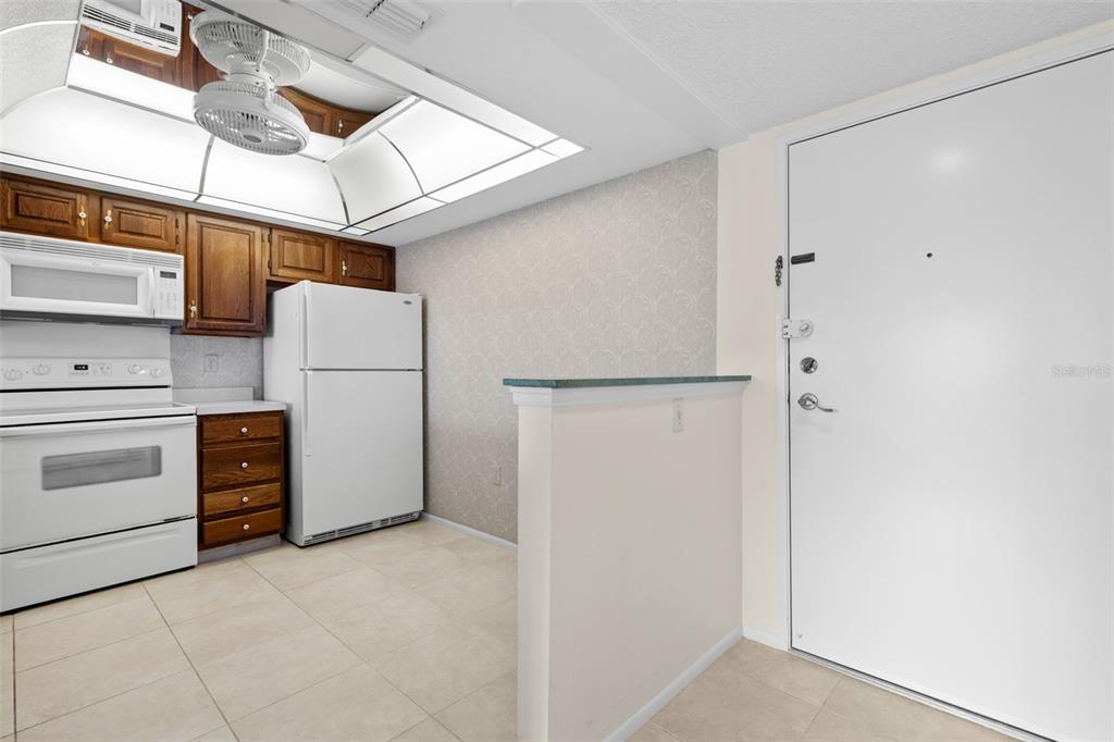 A kitchen features wood cabinets, white appliances, a tiled floor, and a ceiling fan — 2593 COUNTRYSIDE BOULEVARD UNIT 7304, CLEARWATER, FL