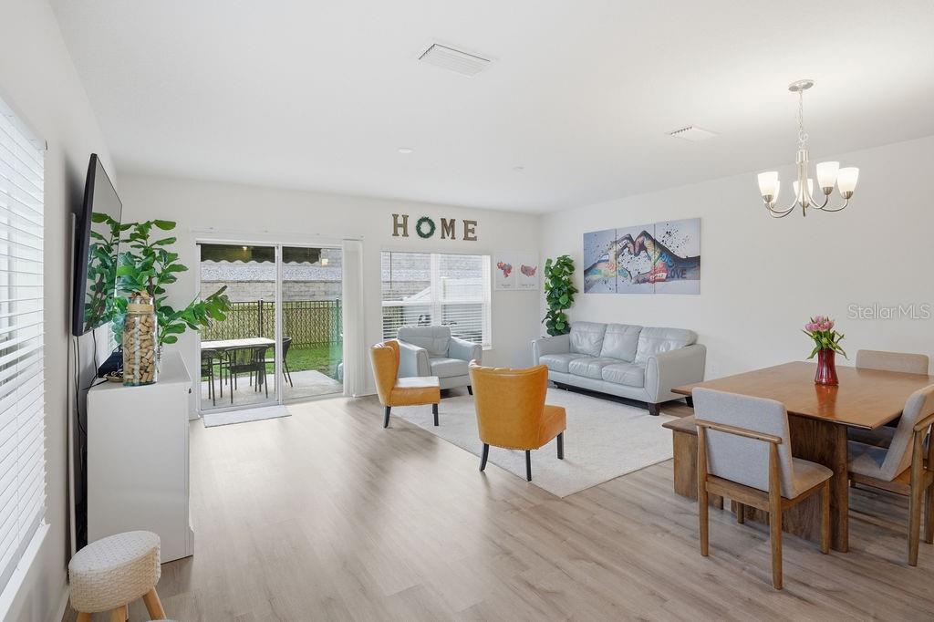 A bright, open-concept living and dining area features light wood flooring and sliding glass doors — 9418 WESTSIDE HILLS DRIVE, DAVENPORT, FL