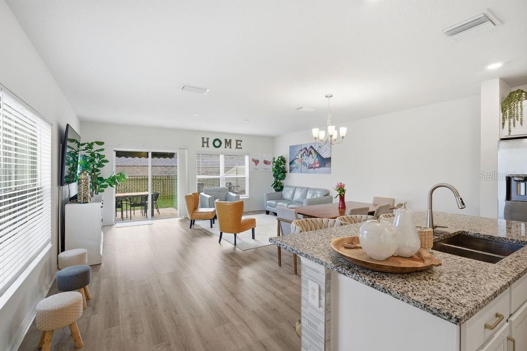 An open-concept living and dining area features light wood flooring, granite countertops, and sliding doors — 9418 WESTSIDE HILLS DRIVE, DAVENPORT, FL