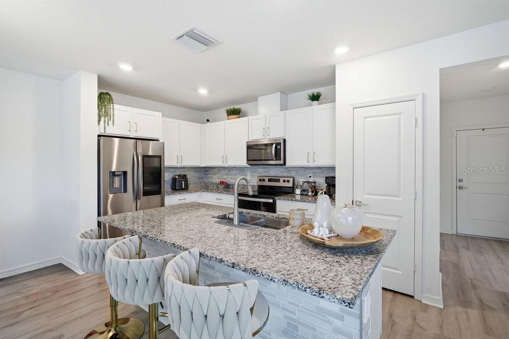 A modern kitchen features white cabinets, granite countertops, a central island, and stainless steel appliances — 9418 WESTSIDE HILLS DRIVE, DAVENPORT, FL