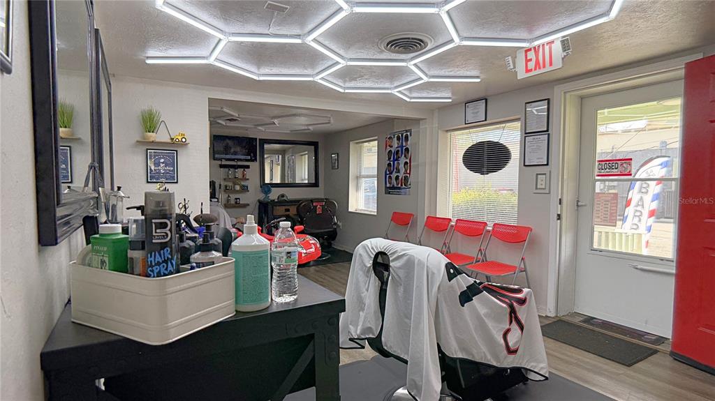 A barbershop interior features a hexagonal ceiling light fixture, a styling chair, and red chairs — 325 NE 25 AVENUE, OCALA, FL