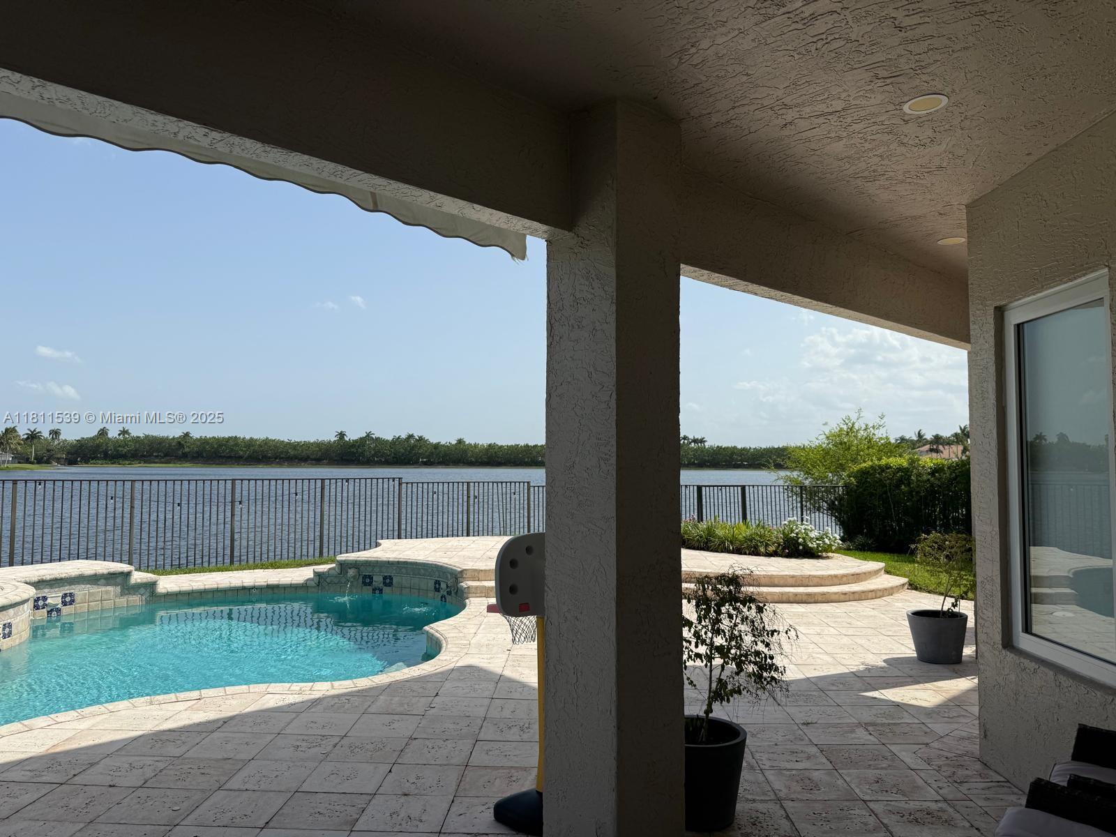 A covered patio overlooks a swimming pool and a lake with a metal fence — 1418 Lantana Dr, Weston FL 33326, WESTON, FL