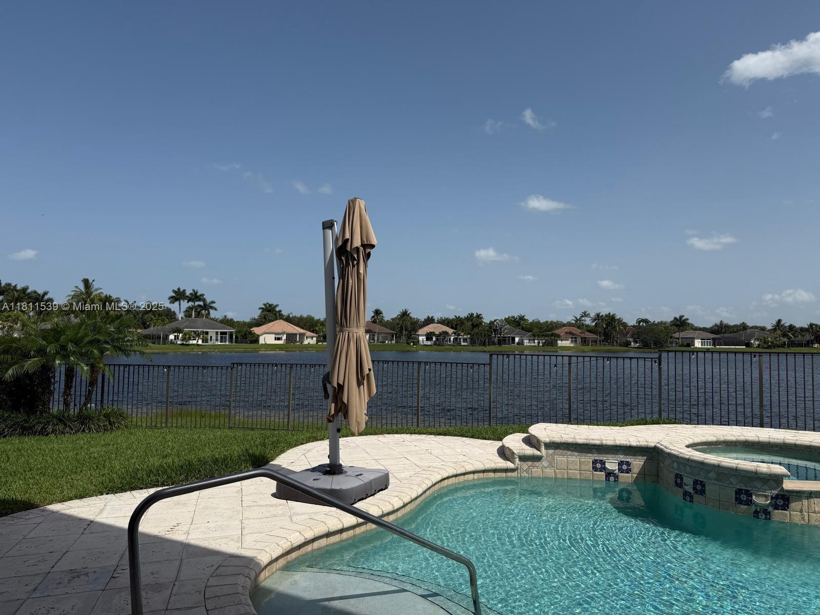 A swimming pool and spa overlook a lake with houses in the background — 1418 Lantana Dr, Weston FL 33326, WESTON, FL