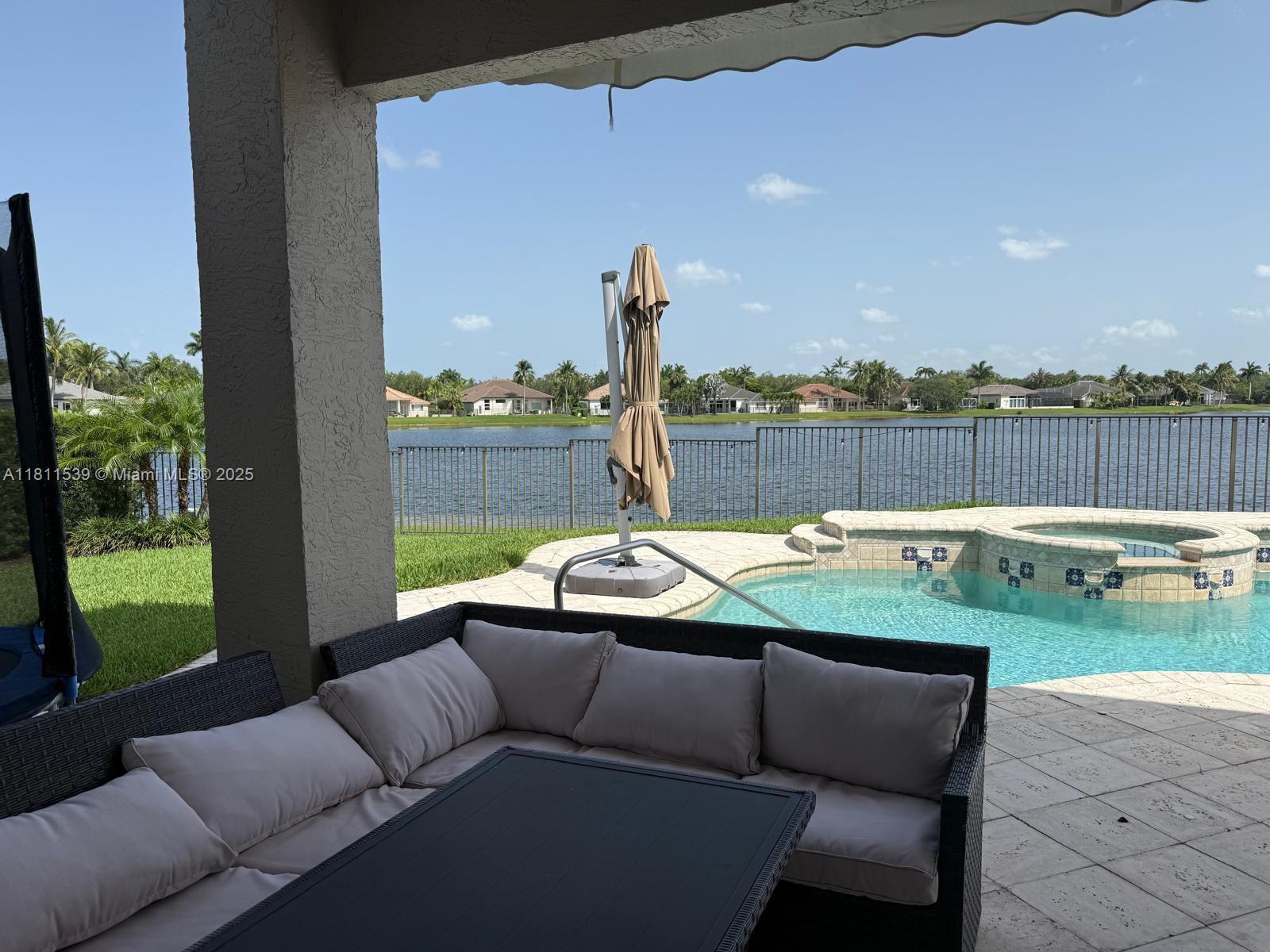 A covered patio features outdoor seating overlooking a swimming pool, spa, and a lake — 1418 Lantana Dr, Weston FL 33326, WESTON, FL