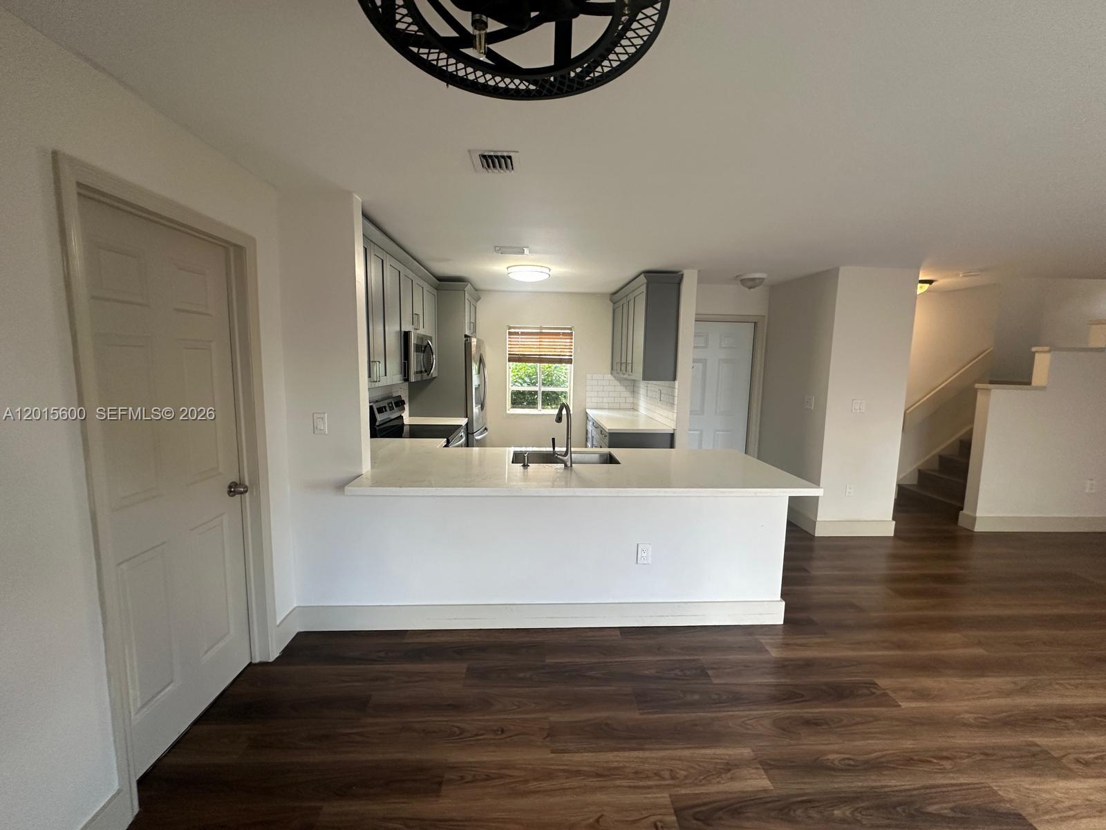 A kitchen with gray cabinets, white countertops, and wood-look flooring opens to a living area — 9062 SW 147th Ct, Miami FL 33196, MIAMI, FL