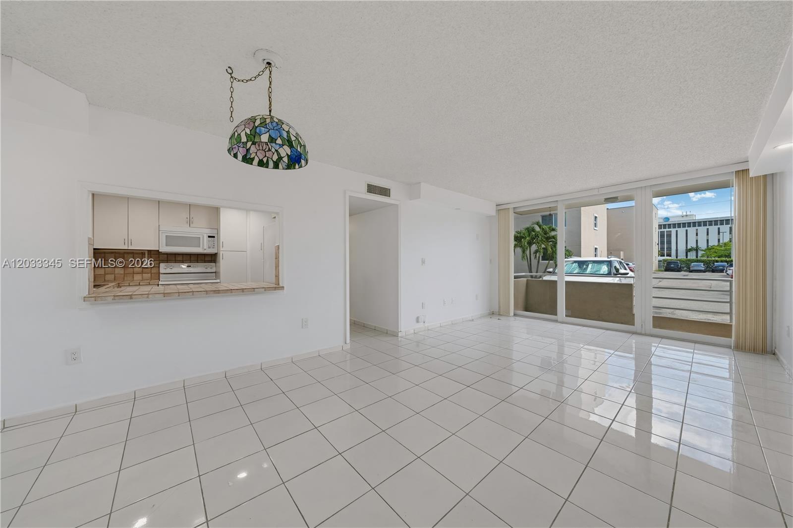 A bright, tiled living area features a kitchen pass-through window and sliding glass balcony doors — 8050 NW 8th St # 110, Miami FL 33126, MIAMI, FL