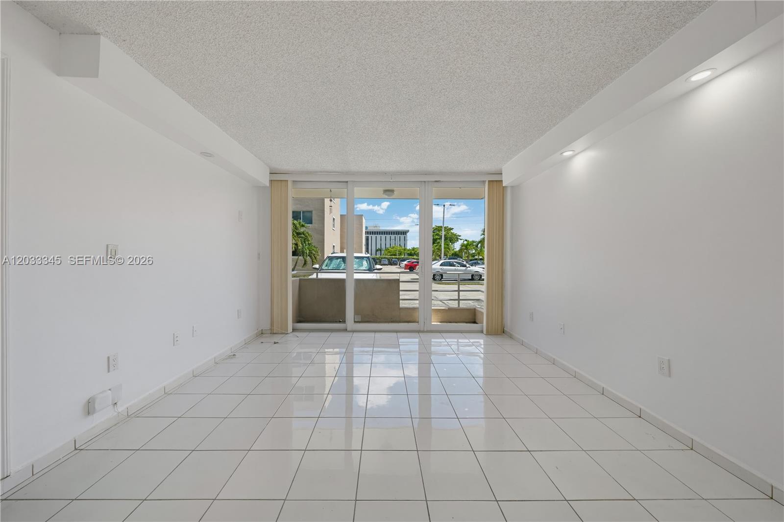 A bright, empty room features white tiled floors, white walls, and sliding glass balcony doors — 8050 NW 8th St # 110, Miami FL 33126, MIAMI, FL