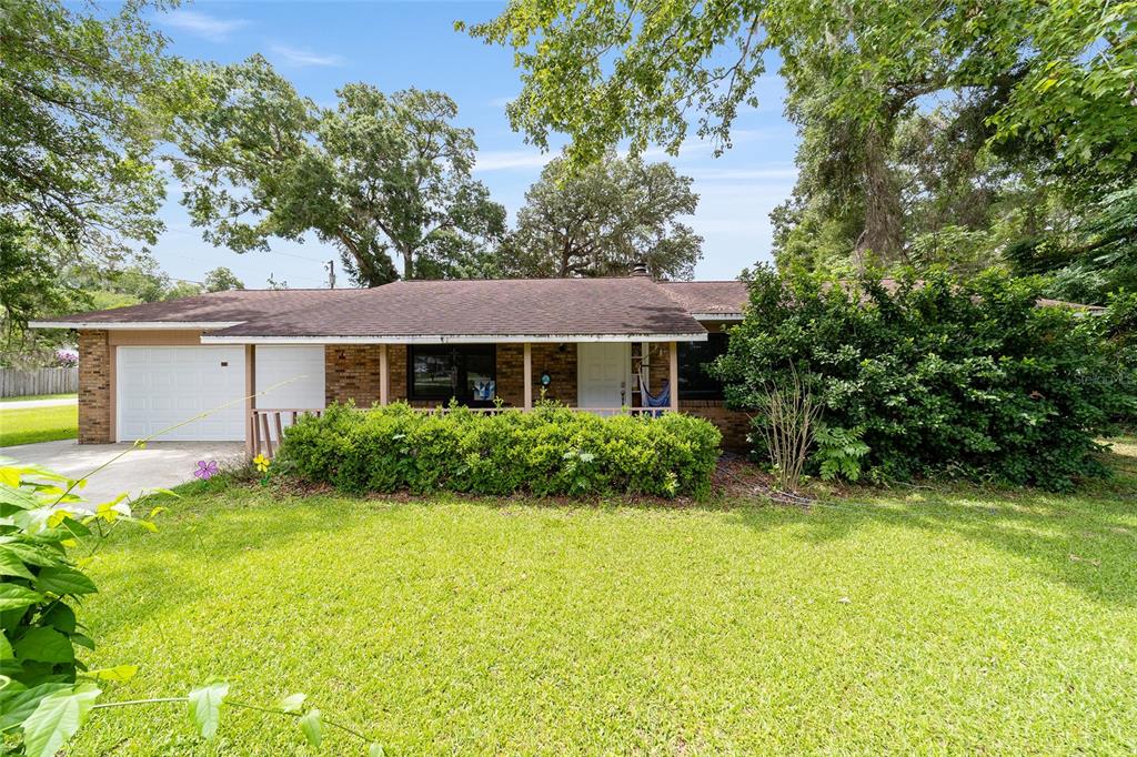 A single-story brick house with a front porch, attached garage, and large surrounding trees — 4170 SE 65TH PLACE, OCALA, FL