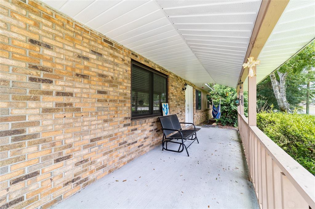 A covered brick porch features a metal glider bench and a wooden railing — 4170 SE 65TH PLACE, OCALA, FL