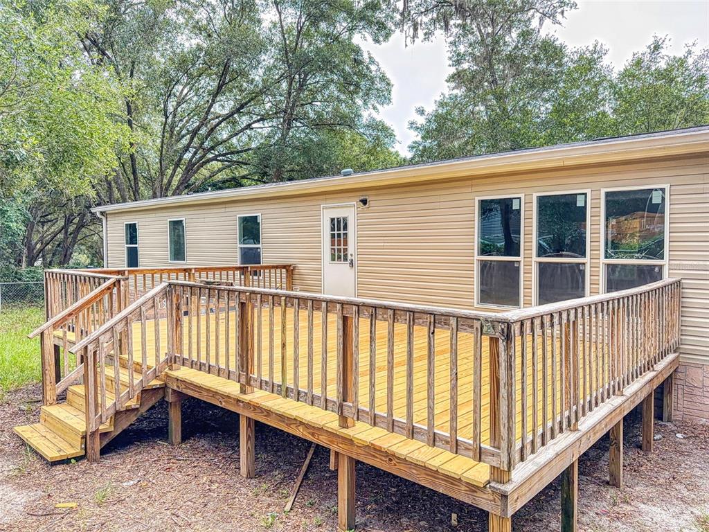 A tan mobile home features a large, elevated wooden deck with railings and stairs — 12841 SE 103RD TERRACE, BELLEVIEW, FL