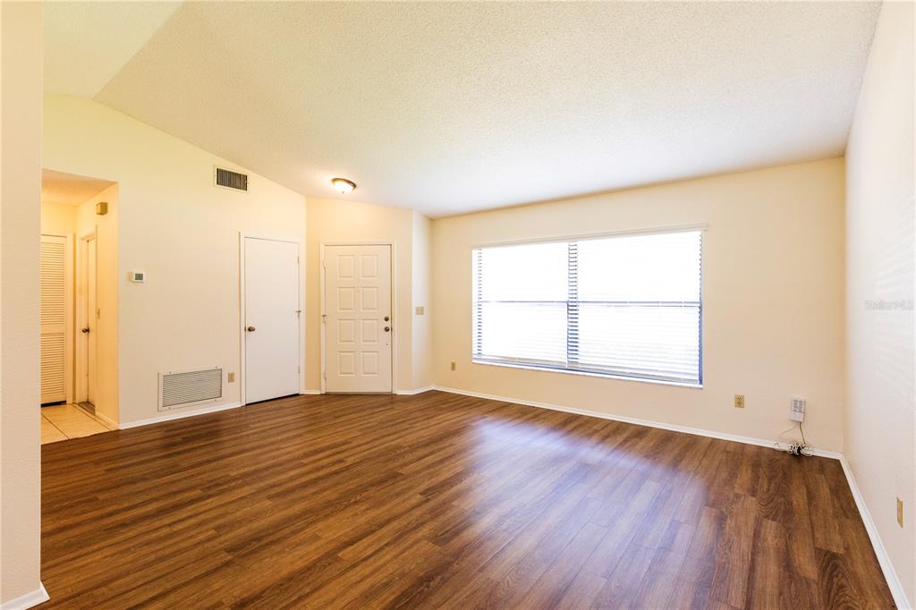 An empty living room features wood-look flooring, light-colored walls, a large window, and two doors — 1002 GAMMAGE POINT, OVIEDO, FL