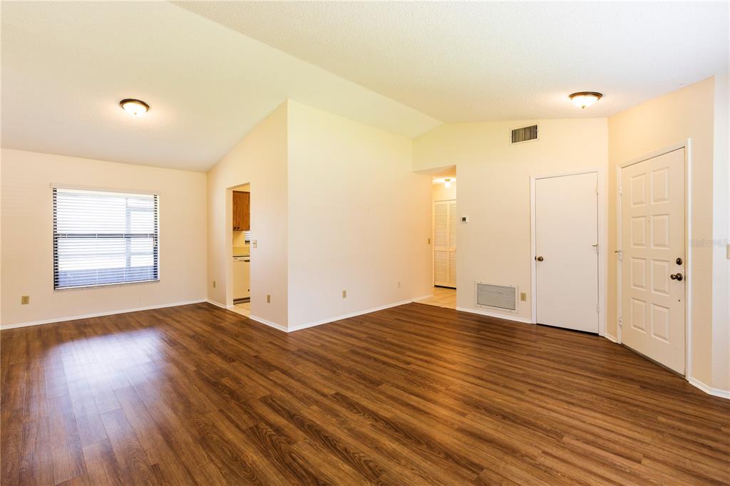 An empty living room with wood-look flooring, vaulted ceilings, and a white entry door — 1002 GAMMAGE POINT, OVIEDO, FL
