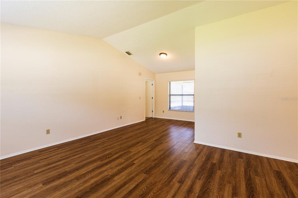 An empty room features light-colored walls, a vaulted ceiling, and dark wood-look flooring — 1002 GAMMAGE POINT, OVIEDO, FL