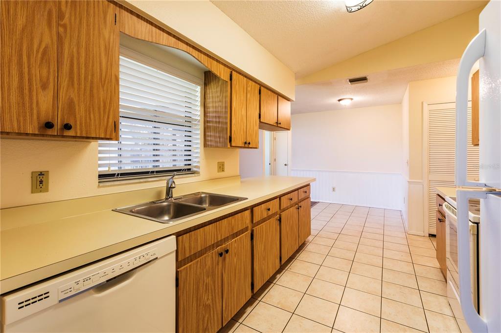A kitchen with wood cabinets, laminate countertops, a double sink, and white tile flooring — 1002 GAMMAGE POINT, OVIEDO, FL