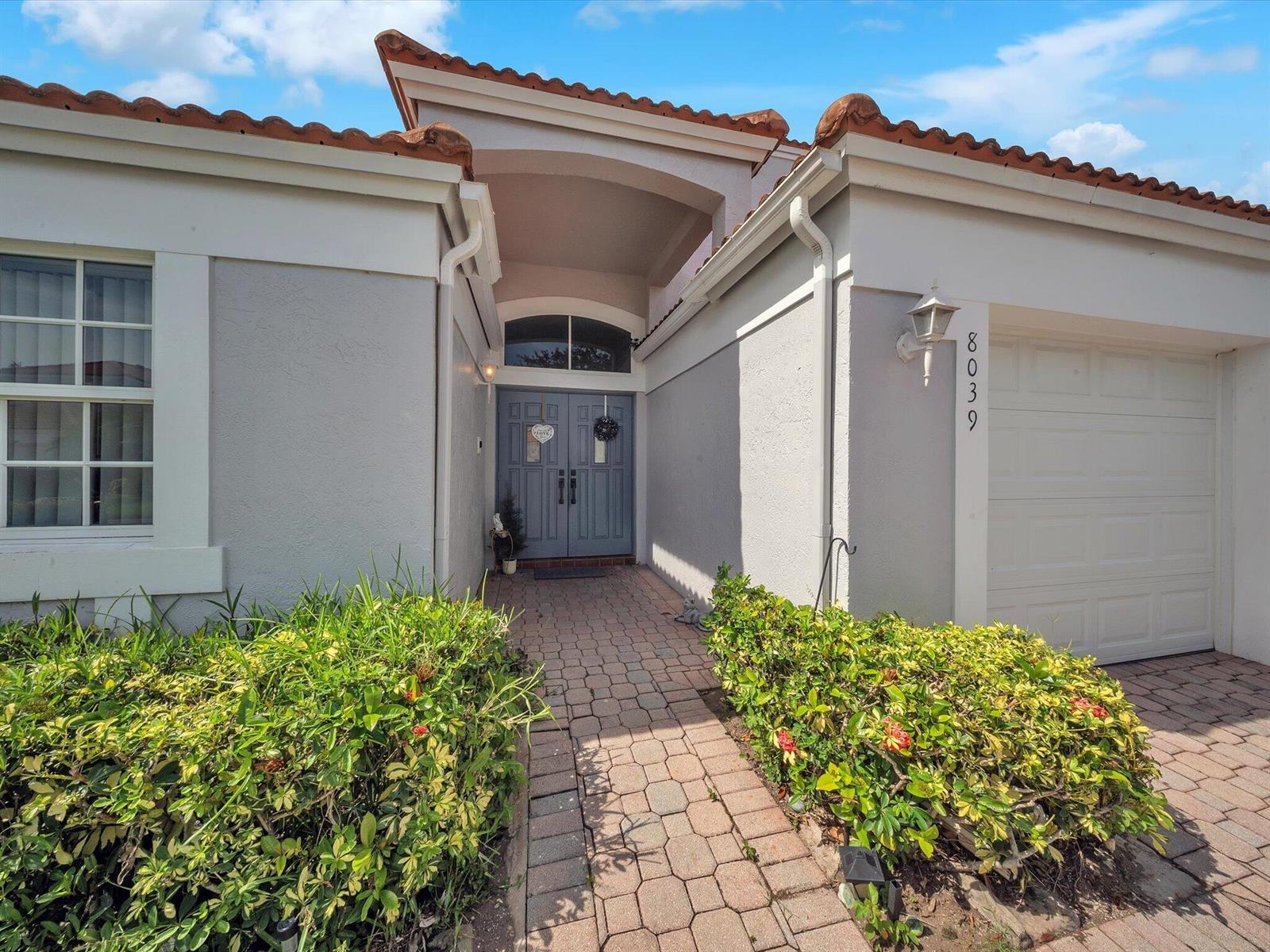 A gray house exterior features a paved walkway leading to a double-door entryway — 8039 N Tranquility Lake Drive, Delray Beach FL 33446, DELRAY BEACH, FL