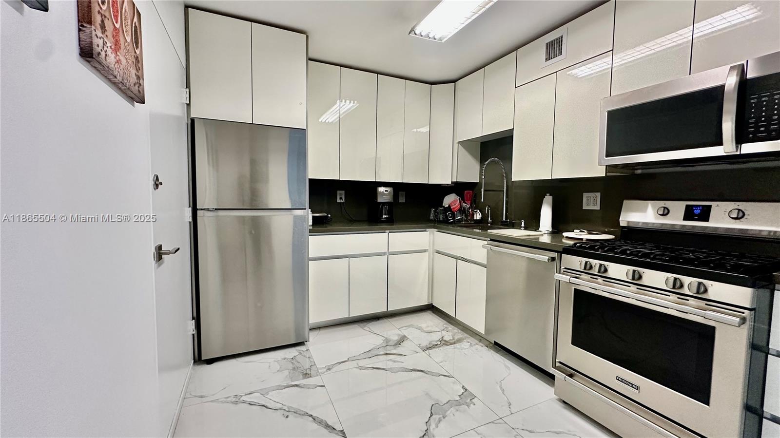 A modern kitchen features white glossy cabinets, stainless steel appliances, and marble-patterned tile flooring — 2030 S Ocean Dr # 1022, Hallandale Beach FL 33009, HALLANDALE BEACH, FL