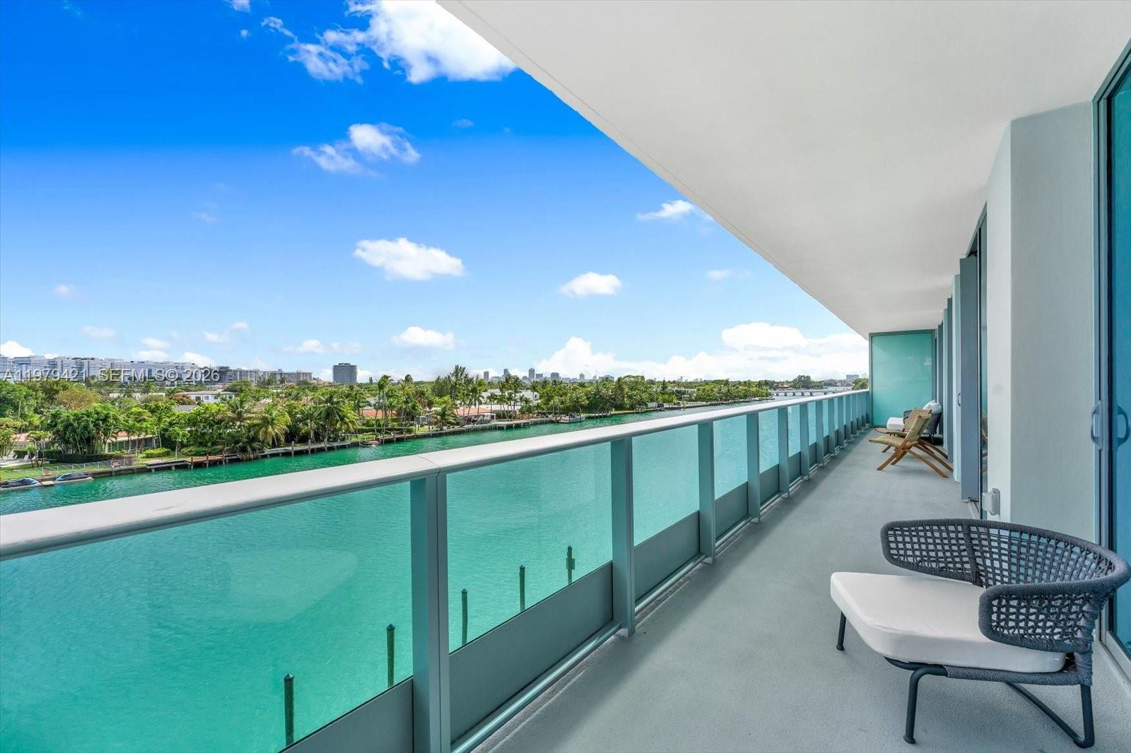 A balcony with a glass railing overlooks a canal and a distant city skyline — 9201 E Bay Harbor Dr # 503, Bal Harbour FL 33154, BAL HARBOUR, FL