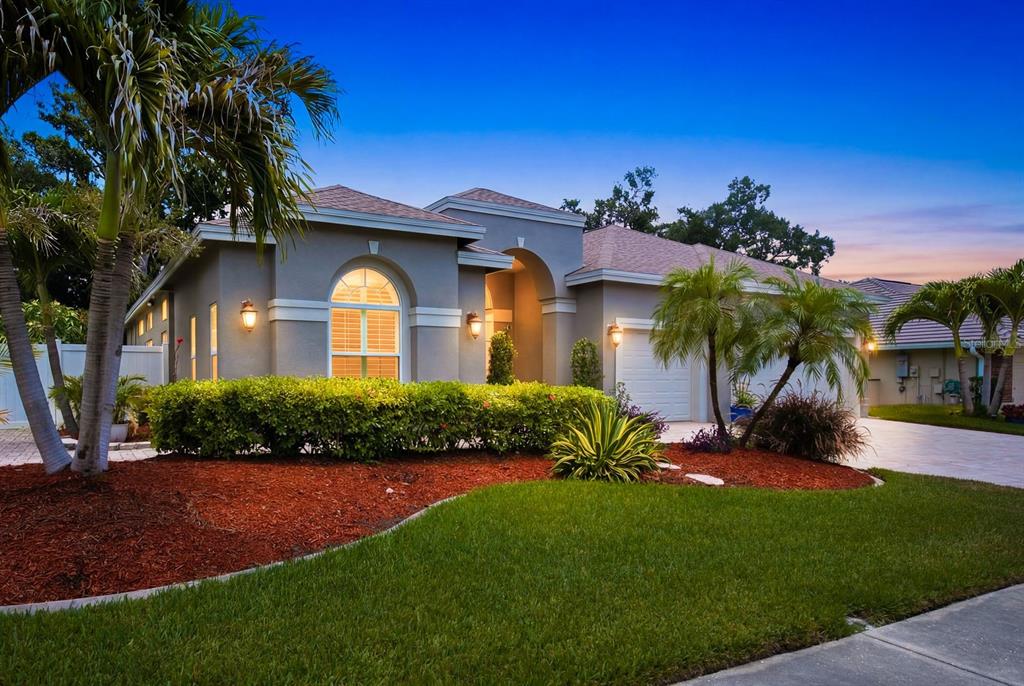A single-story house with a gray stucco exterior, arched window, and landscaped front yard — 141 OLD OAK CIRCLE, PALM HARBOR, FL