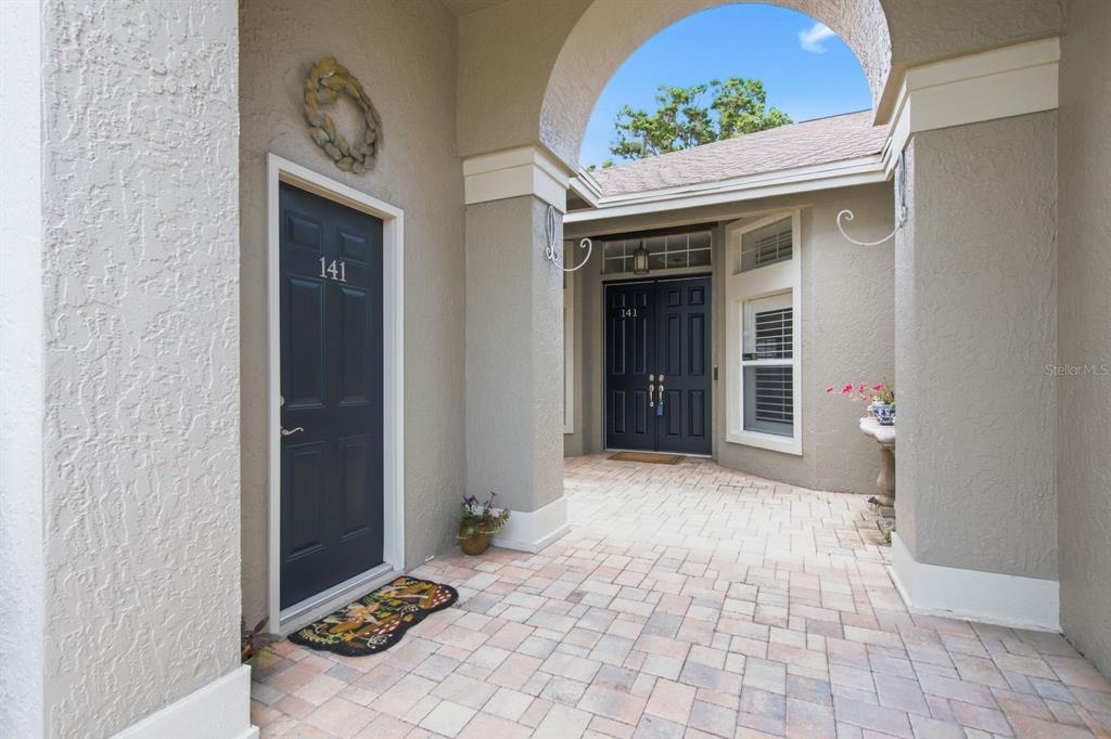 A paved entryway features two dark blue doors labeled 141 under a large arched opening — 141 OLD OAK CIRCLE, PALM HARBOR, FL