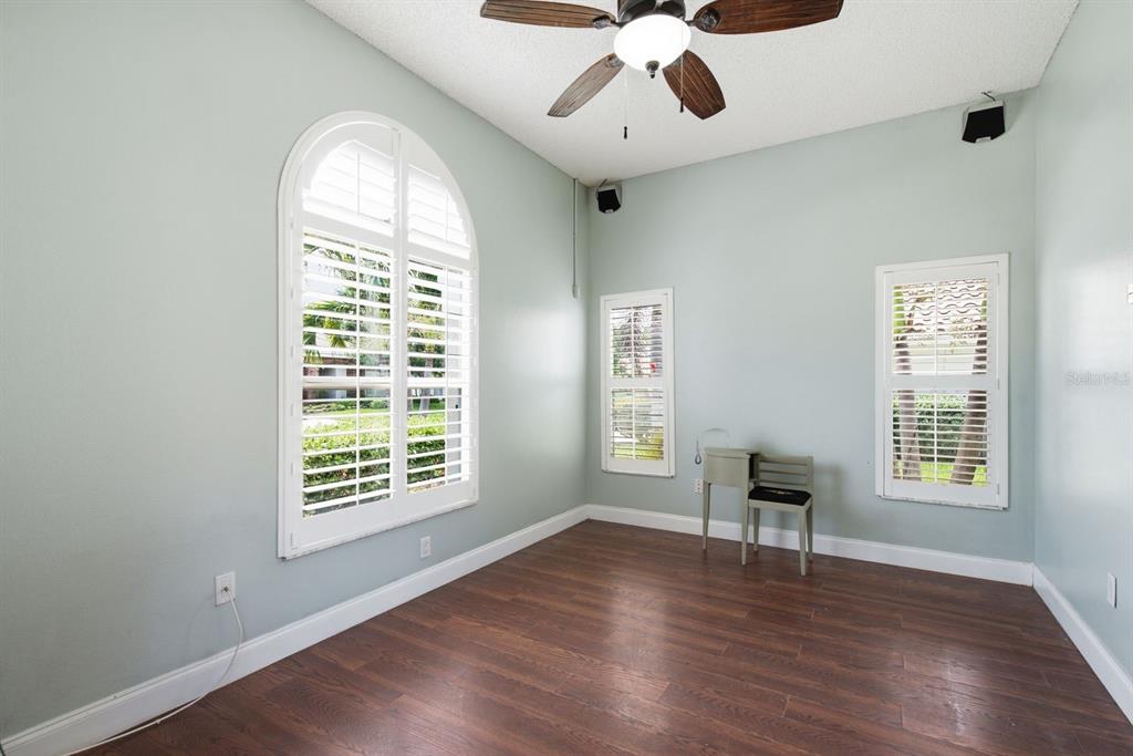 An empty room with light blue walls, dark wood flooring, and three windows with shutters — 141 OLD OAK CIRCLE, PALM HARBOR, FL