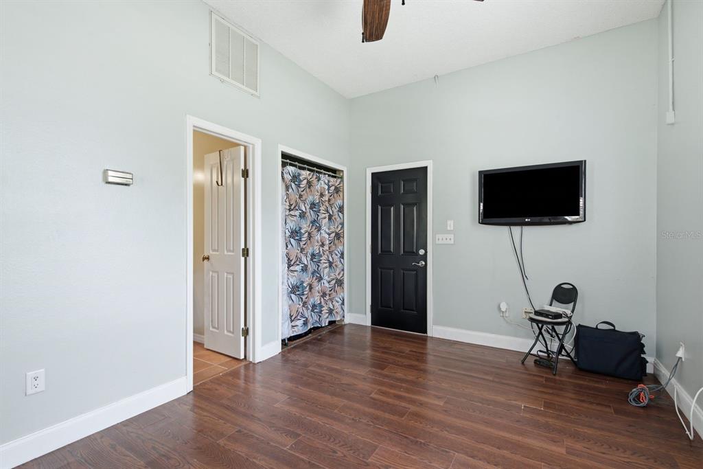 A room with wood-look flooring, a wall-mounted television, a black door, and a closet curtain — 141 OLD OAK CIRCLE, PALM HARBOR, FL