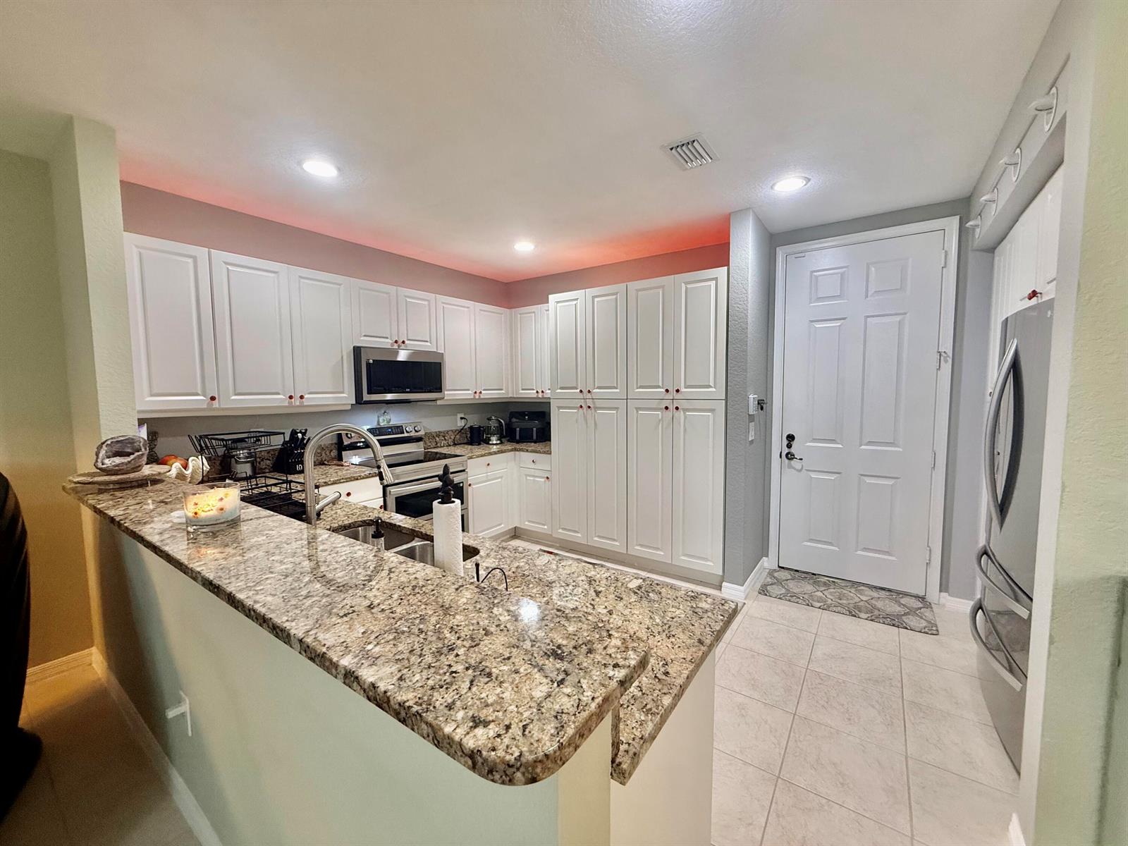 A kitchen features white cabinetry, granite countertops, stainless steel appliances, and a tiled floor — 1015 Ventnor Avenue # 3a, Delray Beach FL 33444, DELRAY BEACH, FL