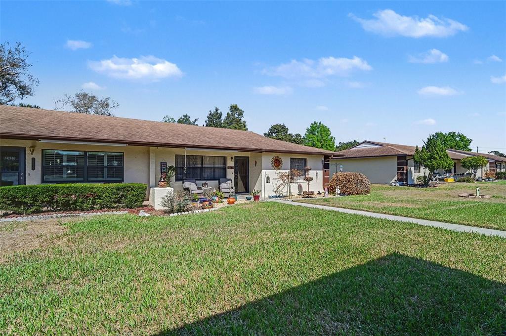 A single-story duplex with a tan stucco exterior, brown shingle roof, and front lawn — 12435 ORANGEWOOD CIRCLE, TAVARES, FL
