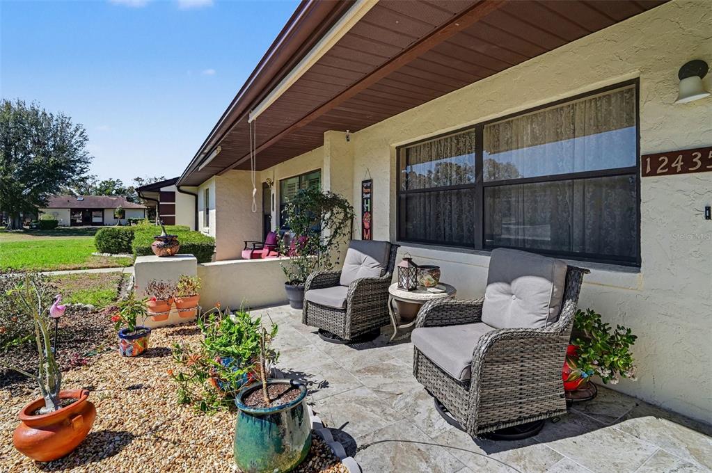 A covered front porch features tiled flooring, wicker chairs, and several potted plants — 12435 ORANGEWOOD CIRCLE, TAVARES, FL