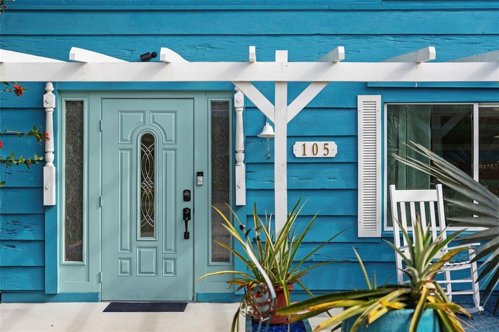 A bright blue house exterior features a light teal front door and a white pergola — 105 TUCKER AVENUE, SARASOTA, FL