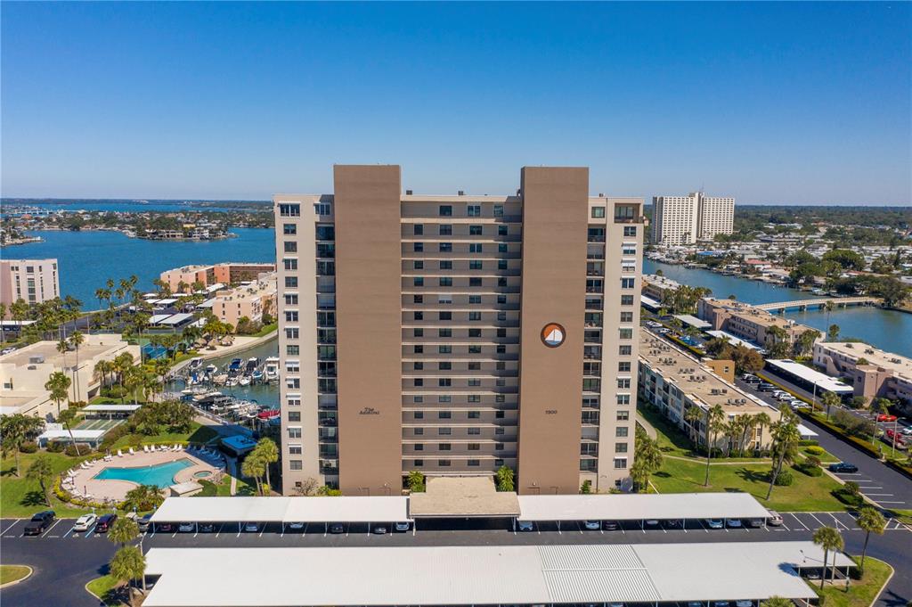 An aerial view shows a tall apartment building with a swimming pool and covered parking — 7300 SUN ISLAND DRIVE S UNIT 602, SOUTH PASADENA, FL