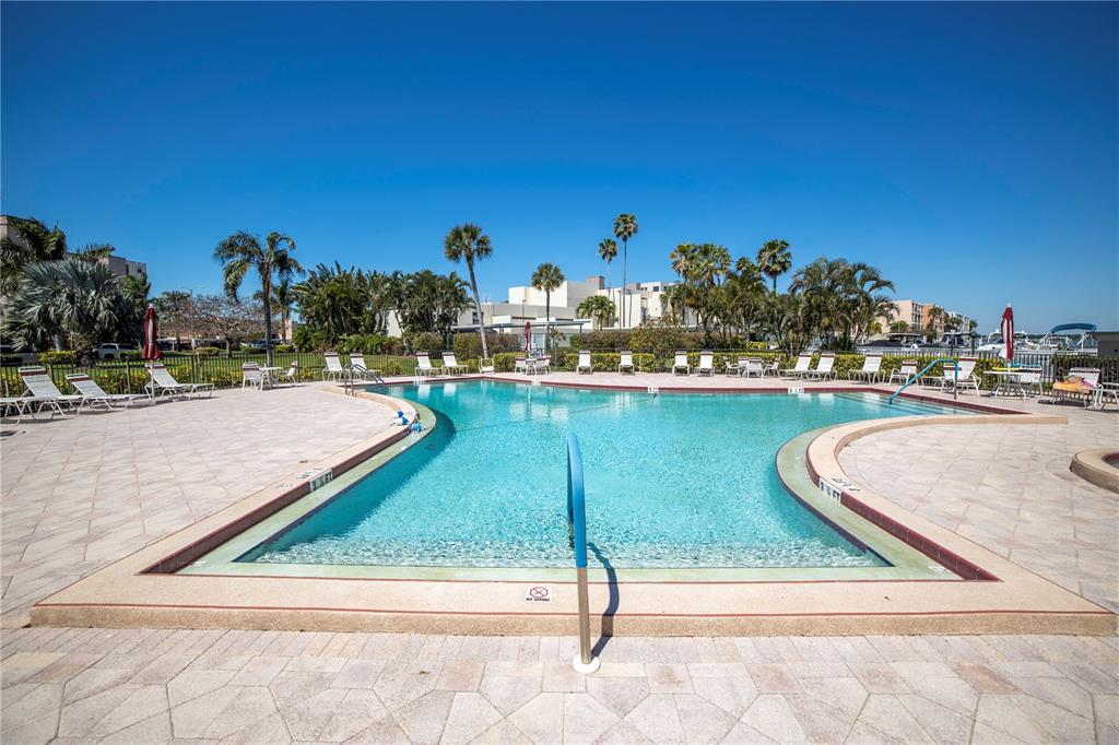 An outdoor swimming pool with lounge chairs on a paved deck under a clear sky — 7300 SUN ISLAND DRIVE S UNIT 602, SOUTH PASADENA, FL