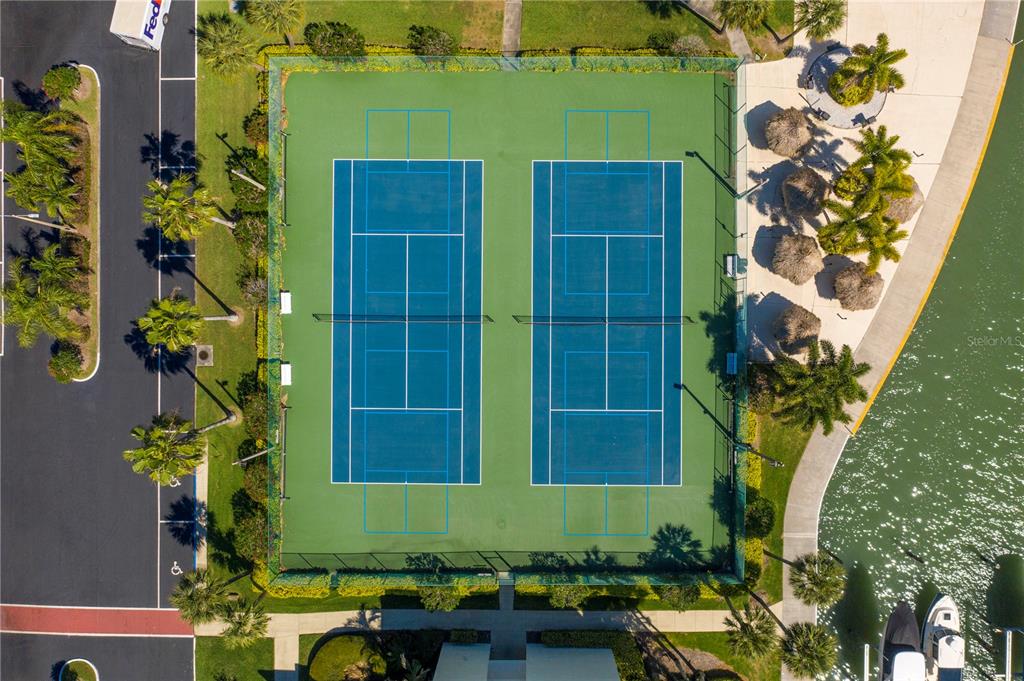 An aerial view shows two blue tennis courts surrounded by a green fence and palm trees — 7300 SUN ISLAND DRIVE S UNIT 602, SOUTH PASADENA, FL