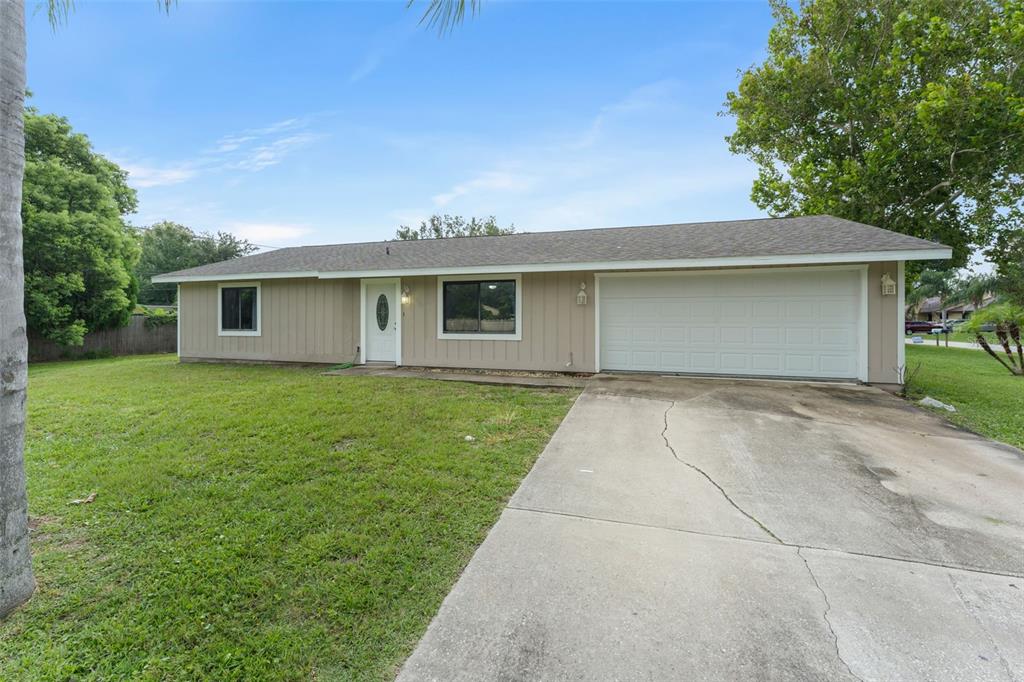 A single-story house with tan siding, a white front door, and an attached two-car garage — 1703 VICTORY PALM DRIVE, EDGEWATER, FL
