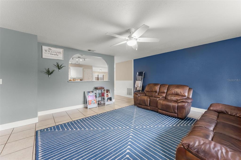 A living room features a blue accent wall, tile flooring, a ceiling fan, and leather sofas — 1703 VICTORY PALM DRIVE, EDGEWATER, FL