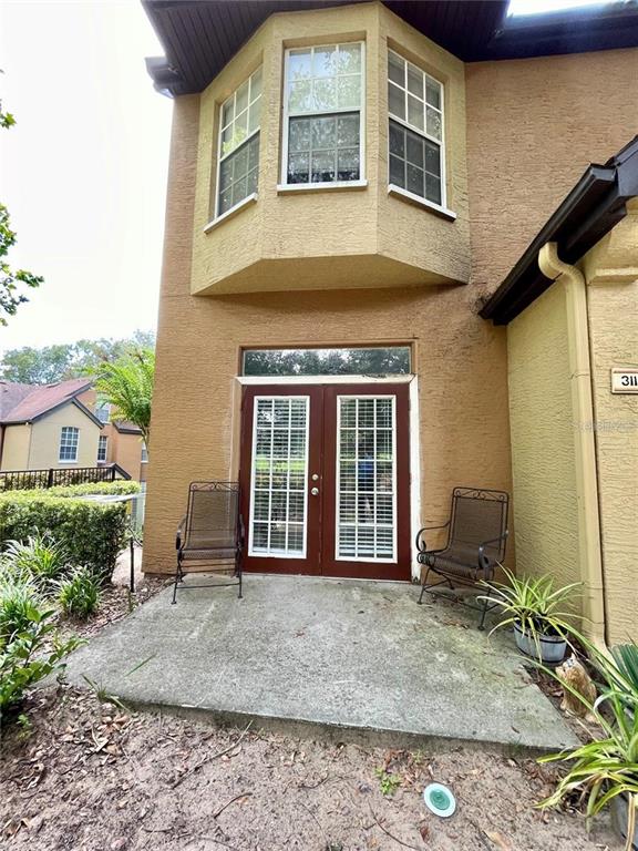 A concrete patio features two metal chairs in front of a house with French doors — 6424 RALEIGH STREET UNIT 3102, ORLANDO, FL