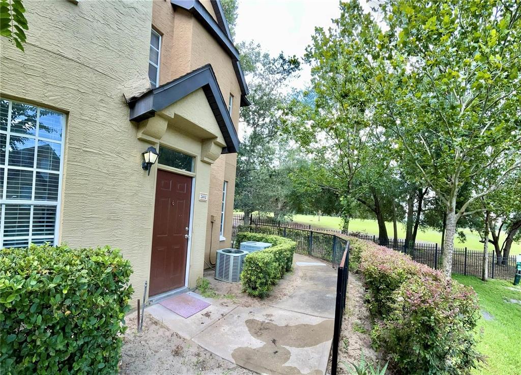 A tan stucco building exterior features a brown front door, a walkway, and landscaping — 6424 RALEIGH STREET UNIT 3102, ORLANDO, FL