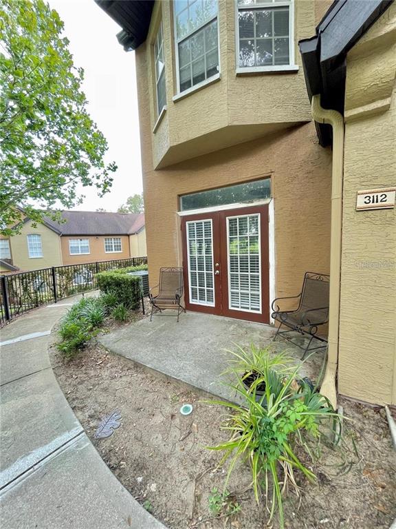 A concrete patio with two chairs sits outside a building with brown stucco walls — 6424 RALEIGH STREET UNIT 3102, ORLANDO, FL