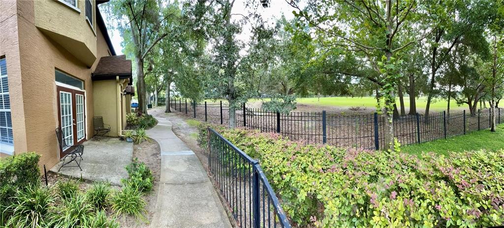 A concrete walkway leads past a tan building exterior toward a fenced grassy area — 6424 RALEIGH STREET UNIT 3102, ORLANDO, FL