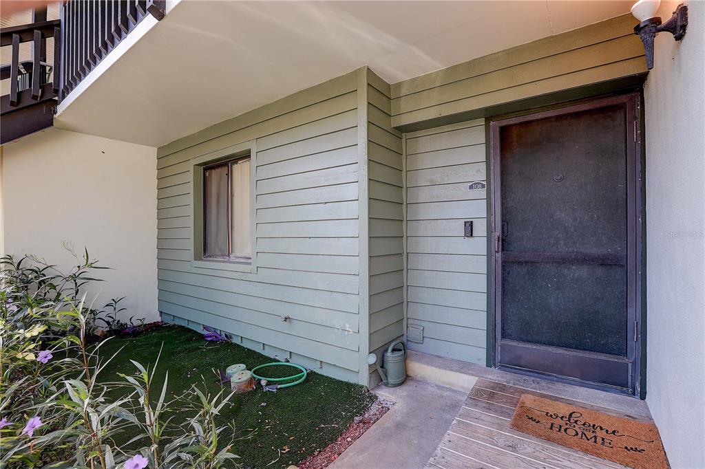 The exterior view shows a green-sided building entrance with a screen door and welcome mat — 3708 GREENERY COURT UNIT 108, TAMPA, FL