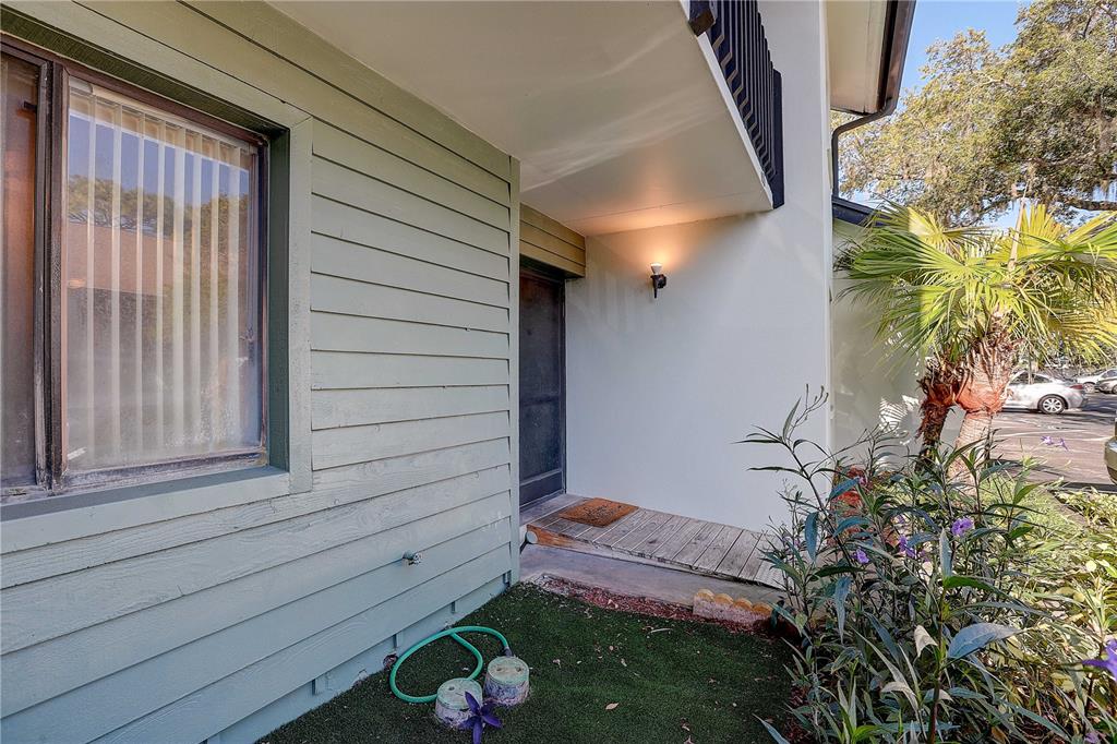 A green-sided house exterior features a small wooden porch, a front door, and landscaping — 3708 GREENERY COURT UNIT 108, TAMPA, FL