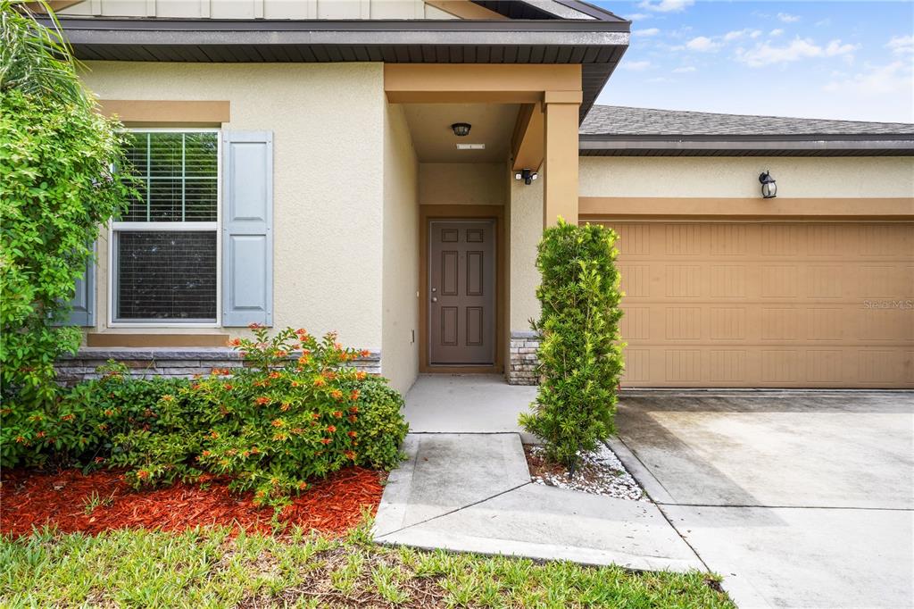 The exterior of a house features a tan garage, a front door, and landscaped bushes — 3004 NEVERLAND DRIVE, NEW SMYRNA BEACH, FL