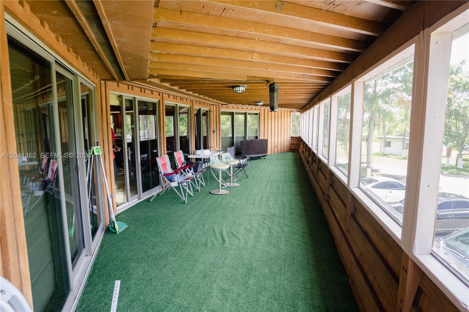 A long, covered porch features green artificial turf flooring, wood-paneled walls, and sliding glass doors — 10337 NE 120TH, Okeechobee FL 34972, OKEECHOBEE, FL