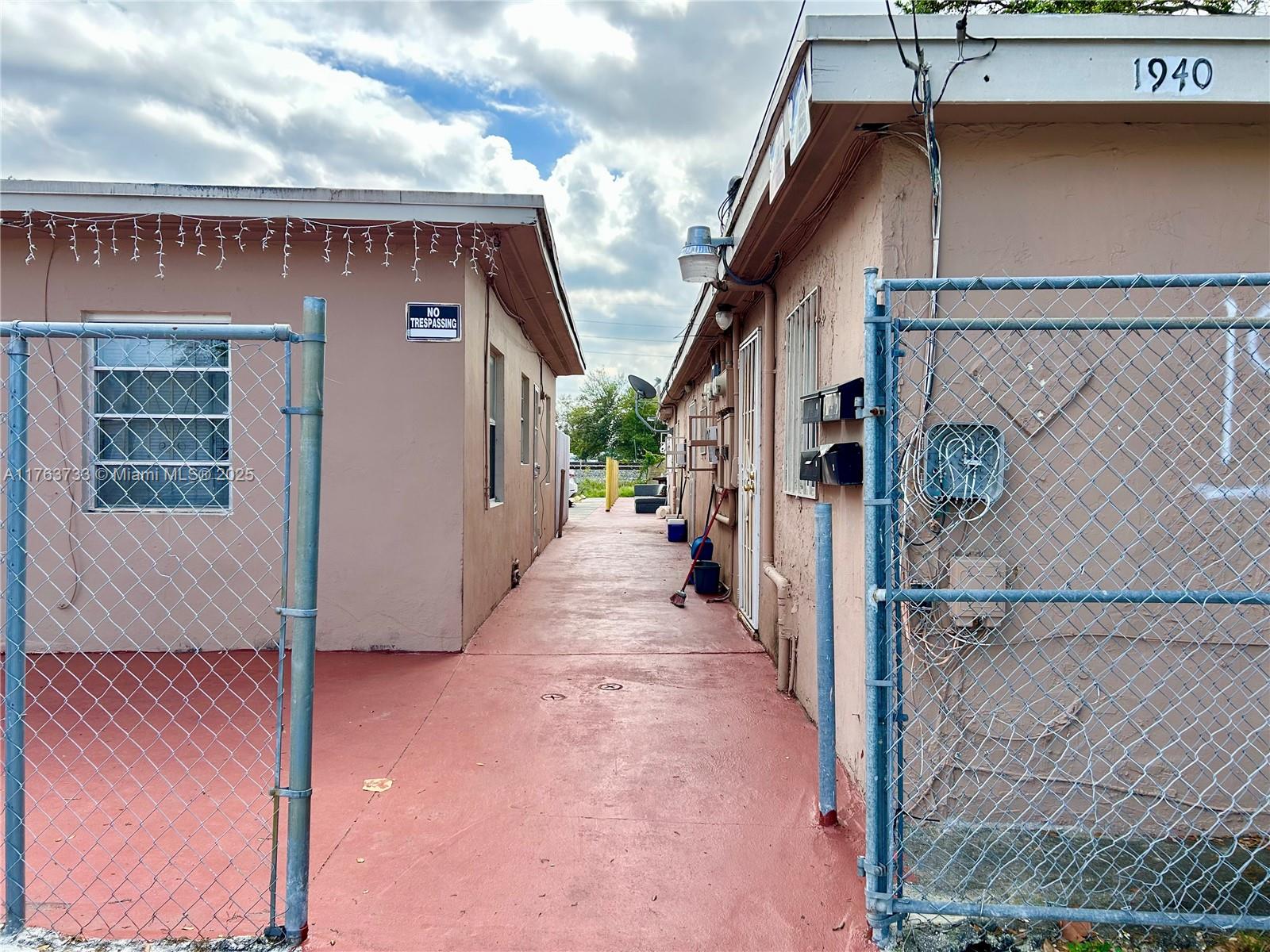 A narrow concrete walkway sits between two tan buildings enclosed by chain-link fencing — 1940 Ali Baba Ave, Opa-Locka FL 33054, OPA-LOCKA, FL