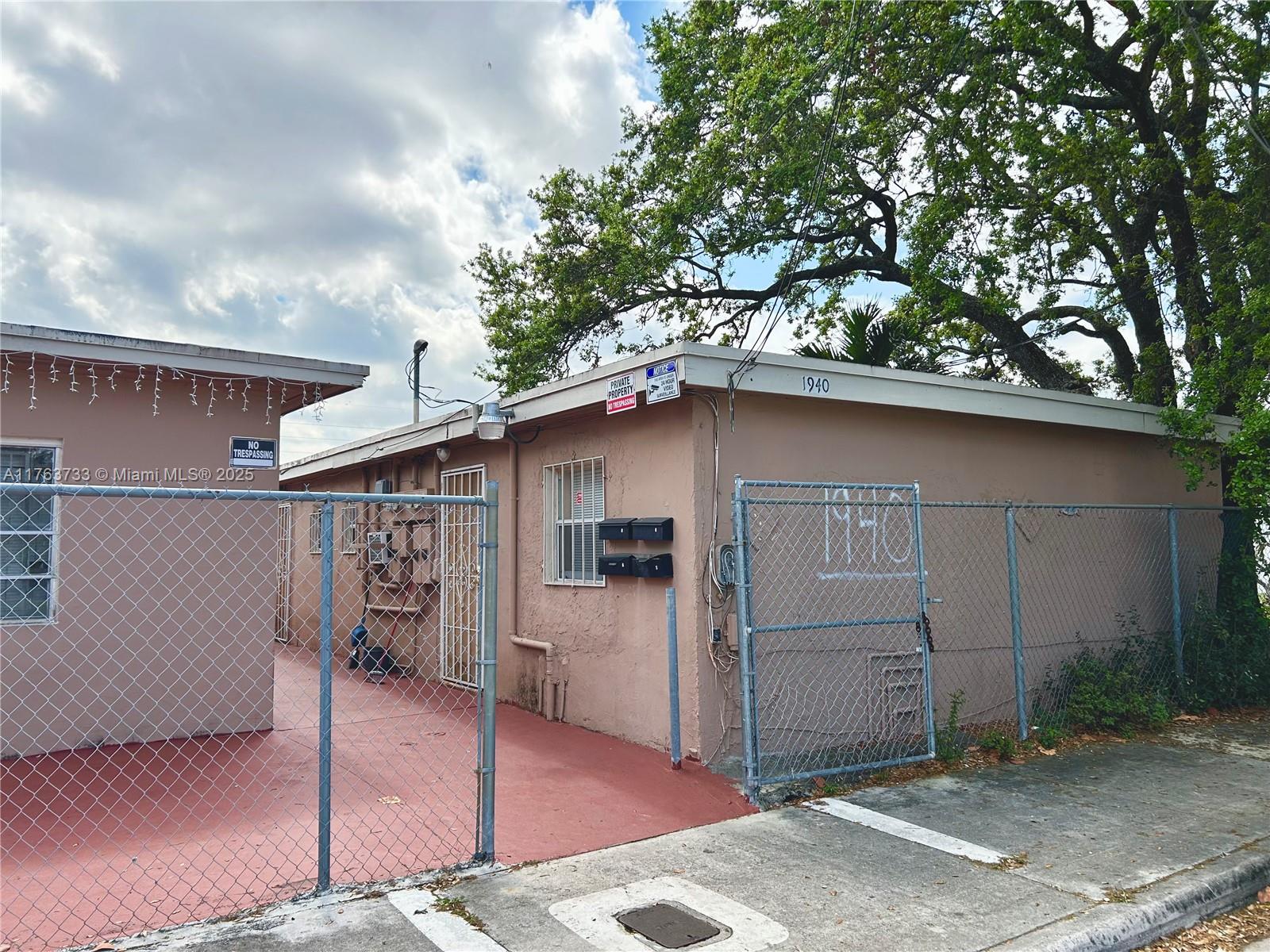 A fenced, single-story tan building with a red concrete patio and multiple mailboxes — 1940 Ali Baba Ave, Opa-Locka FL 33054, OPA-LOCKA, FL