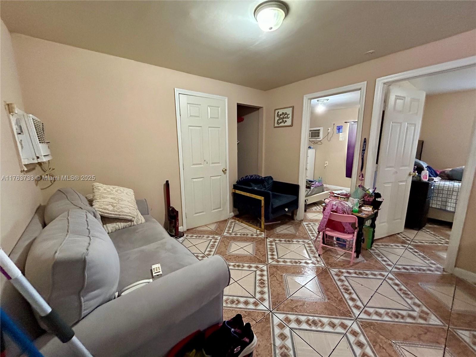 A living room features a grey sofa, tiled floors, and doorways leading to other rooms — 1940 Ali Baba Ave, Opa-Locka FL 33054, OPA-LOCKA, FL