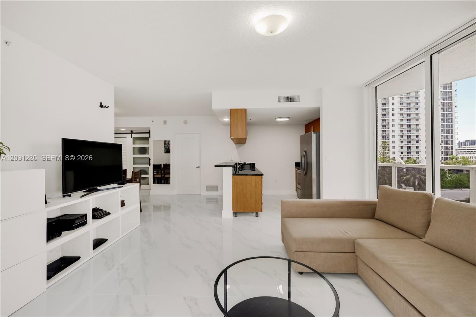 A living room with white marble floors, a beige sectional sofa, and an open kitchen — 601 NE 23rd St # 706, Miami FL 33137, MIAMI, FL