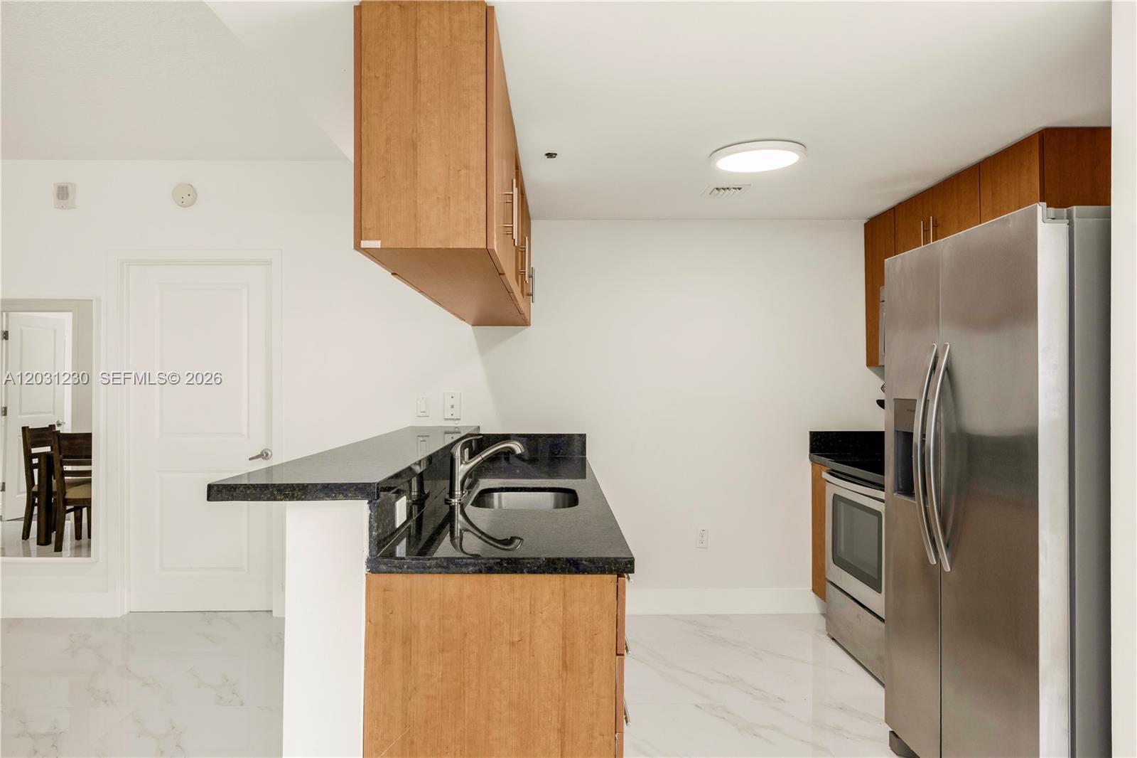 A kitchen features wood cabinets, black granite countertops, stainless steel appliances, and white flooring — 601 NE 23rd St # 706, Miami FL 33137, MIAMI, FL