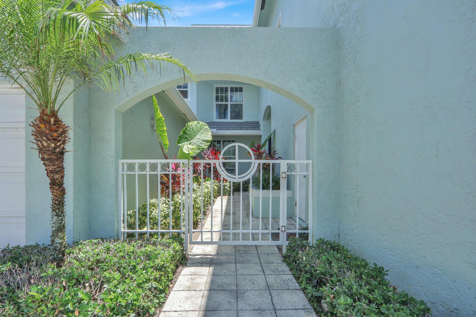 A white metal gate stands at the entrance of a light blue stucco house courtyard — 1506 Mizzenmast Way, Jupiter FL 33477, JUPITER, FL