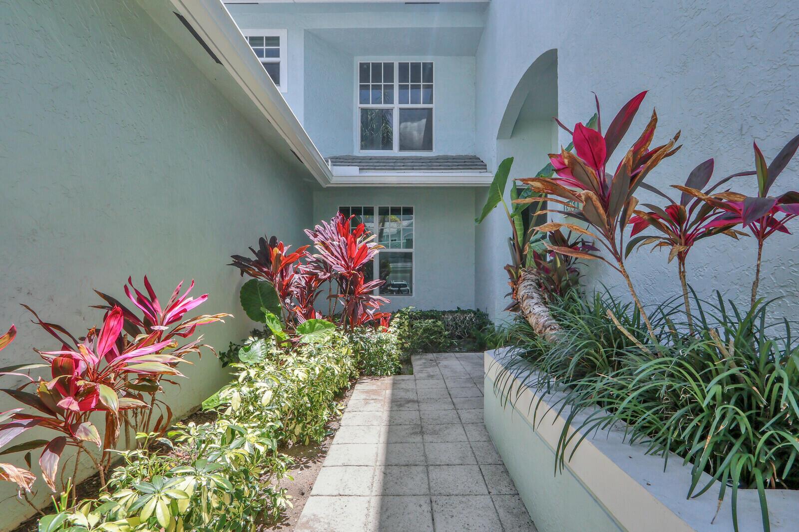 A paved walkway leads to the entrance of a light blue house with tropical landscaping — 1506 Mizzenmast Way, Jupiter FL 33477, JUPITER, FL