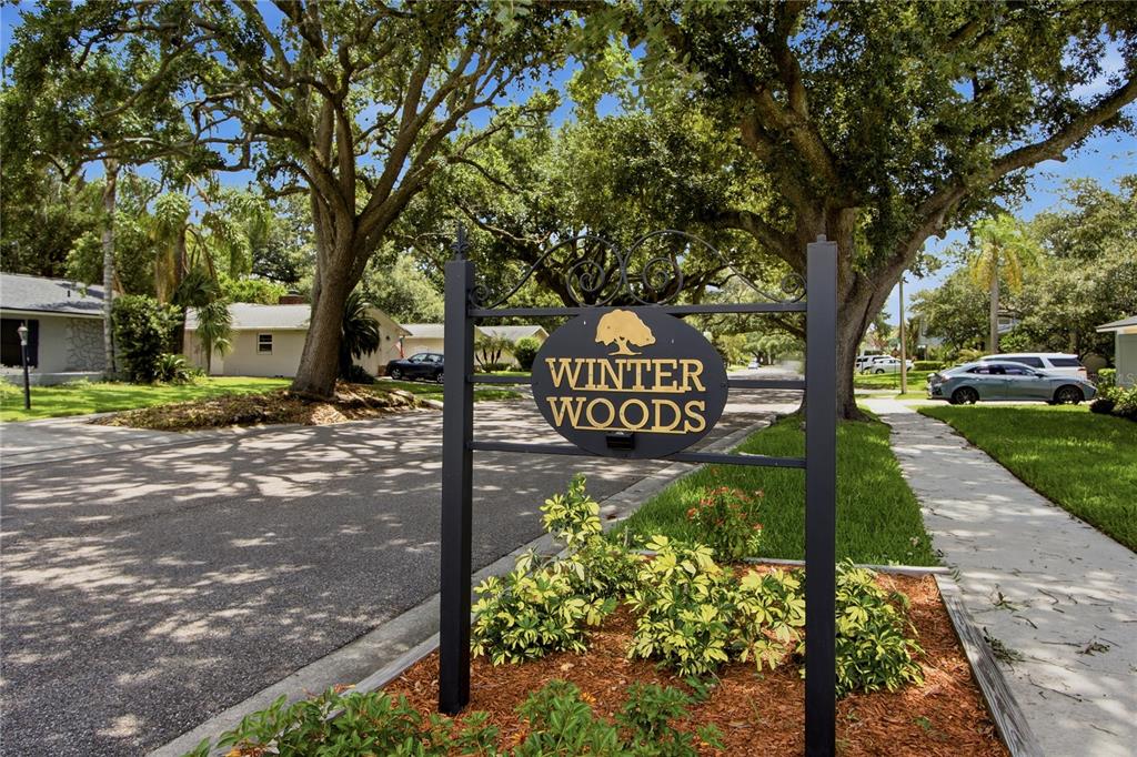 A black metal sign reading Winter Woods stands in a landscaped area near a street — 2028 SUSSEX ROAD, WINTER PARK, FL